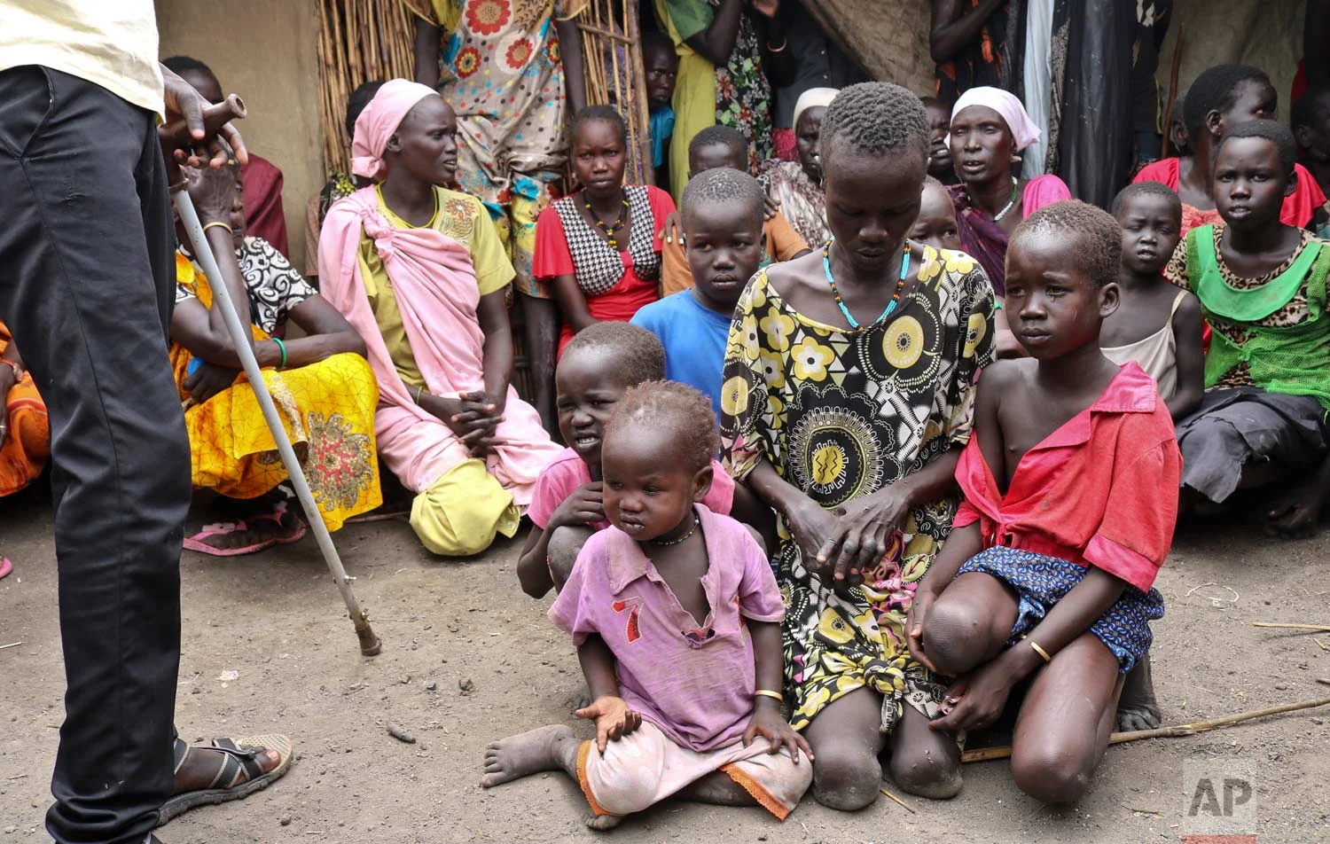 In this photo taken Friday, May 26, 2017, mother Nyayan Koang, who is unable to stand up due to polio, sits with her other children minutes after being reunited with her son James, a former child soldier walking with a crutch, left, and saw him for the first time in 3 years, in Bentiu, South Sudan. (AP Photo/Sam Mednick)