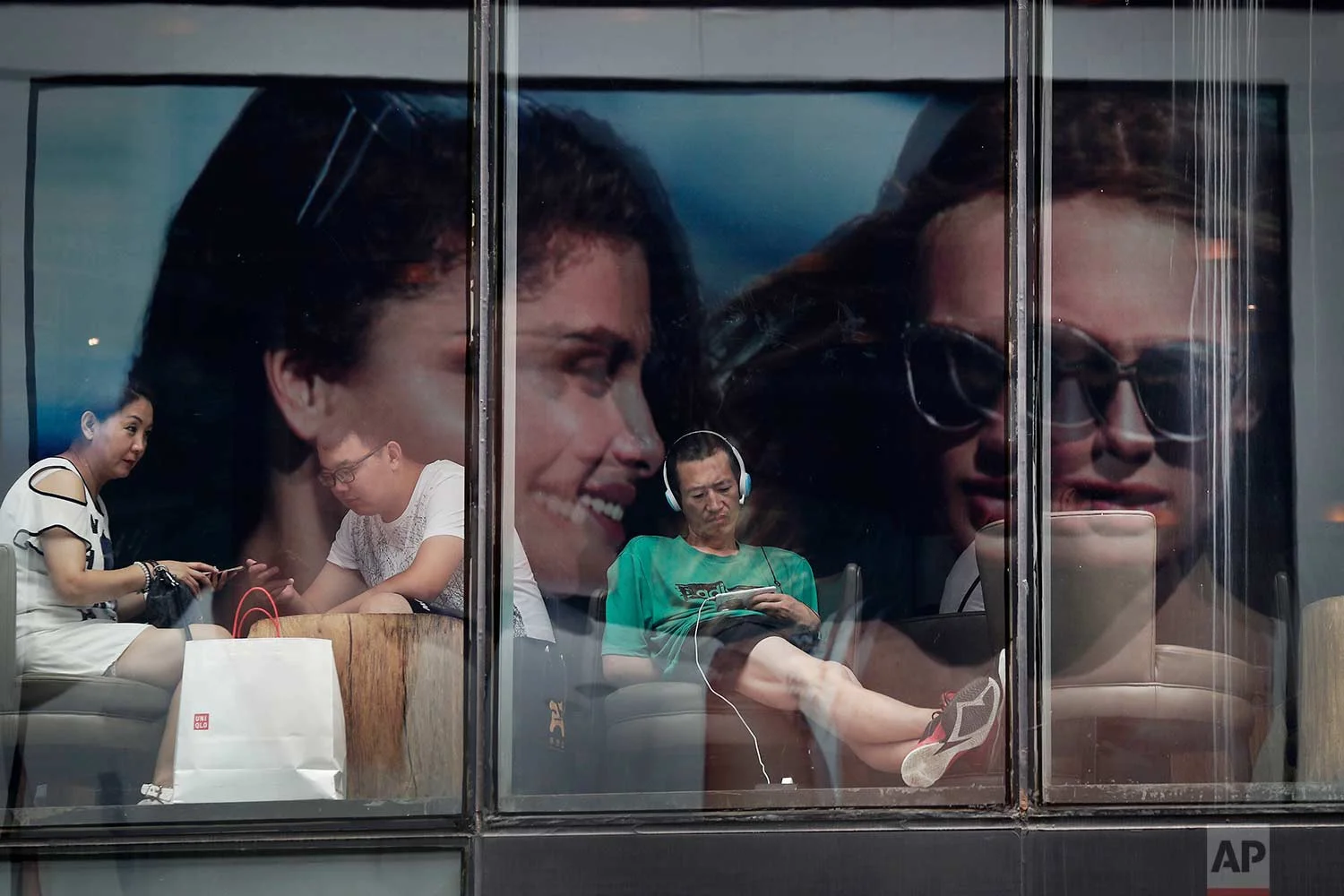 With a fashion advertisement billboard reflected in the windows, people spend time in a cafe at a shopping mall in Beijing, on Monday, July 17, 2017. (AP Photo/Andy Wong)