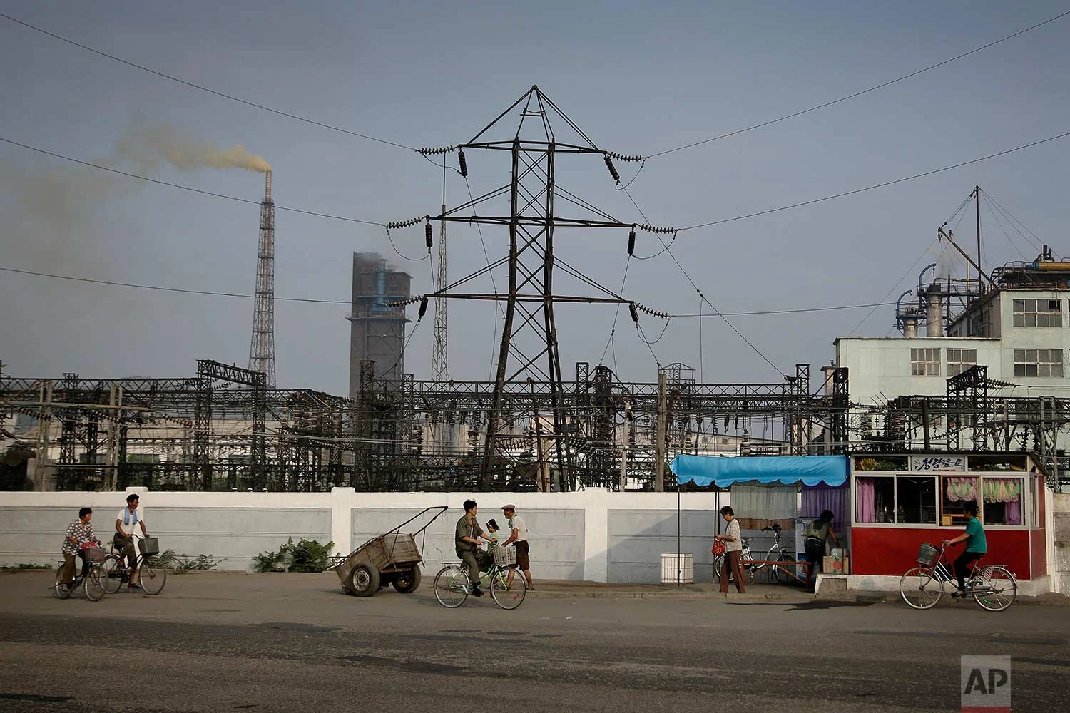 In this Thursday, July 20, 2017, photo, North Koreans cycle while others walk past a fertilizer plant in Hamhung, North Korea's second-largest city. (AP Photo/Wong Maye-E)