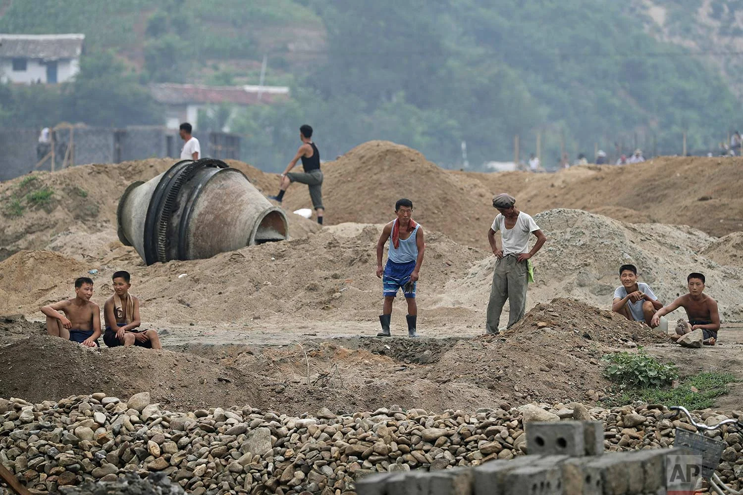 In this Friday, July 21, 2017, photo, men and boys rest at a construction site on the outskirts of Hamhung, North Korea's second-largest city, where construction workers unearthed a rusted but still potentially deadly mortar round in February. (AP Photo/Wong Maye-E)