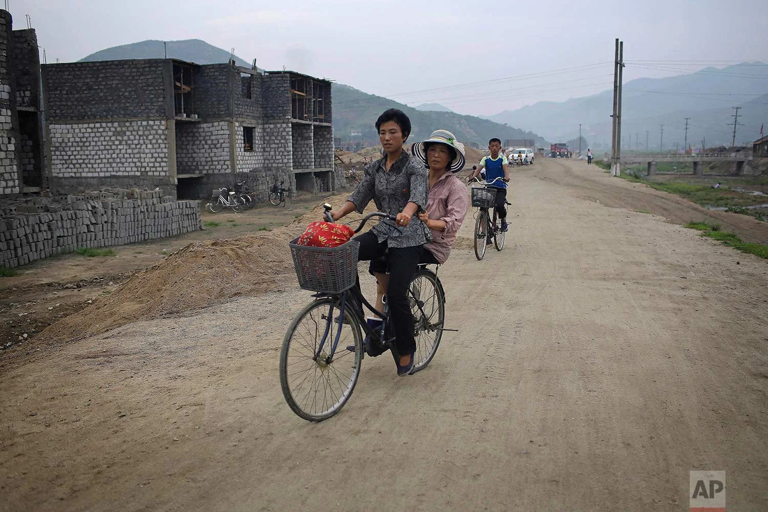 In this Friday, July 21, 2017, photo, women cycle past a construction site on the outskirts of Hamhung, North Korea's second-largest city, where construction workers unearthed a rusted but still potentially deadly mortar round in February. (AP Photo/Wong Maye-E)