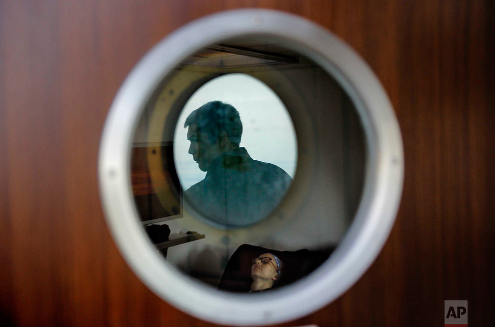  In this Thursday, July 13, 2017 photo, trainee David Kullualik is reflected in a deck door window looking out to sea as researcher Ilona Mettiainen reclines in a massage chair aboard the Finnish icebreaker MSV Nordica as it sails the Bering Sea to t
