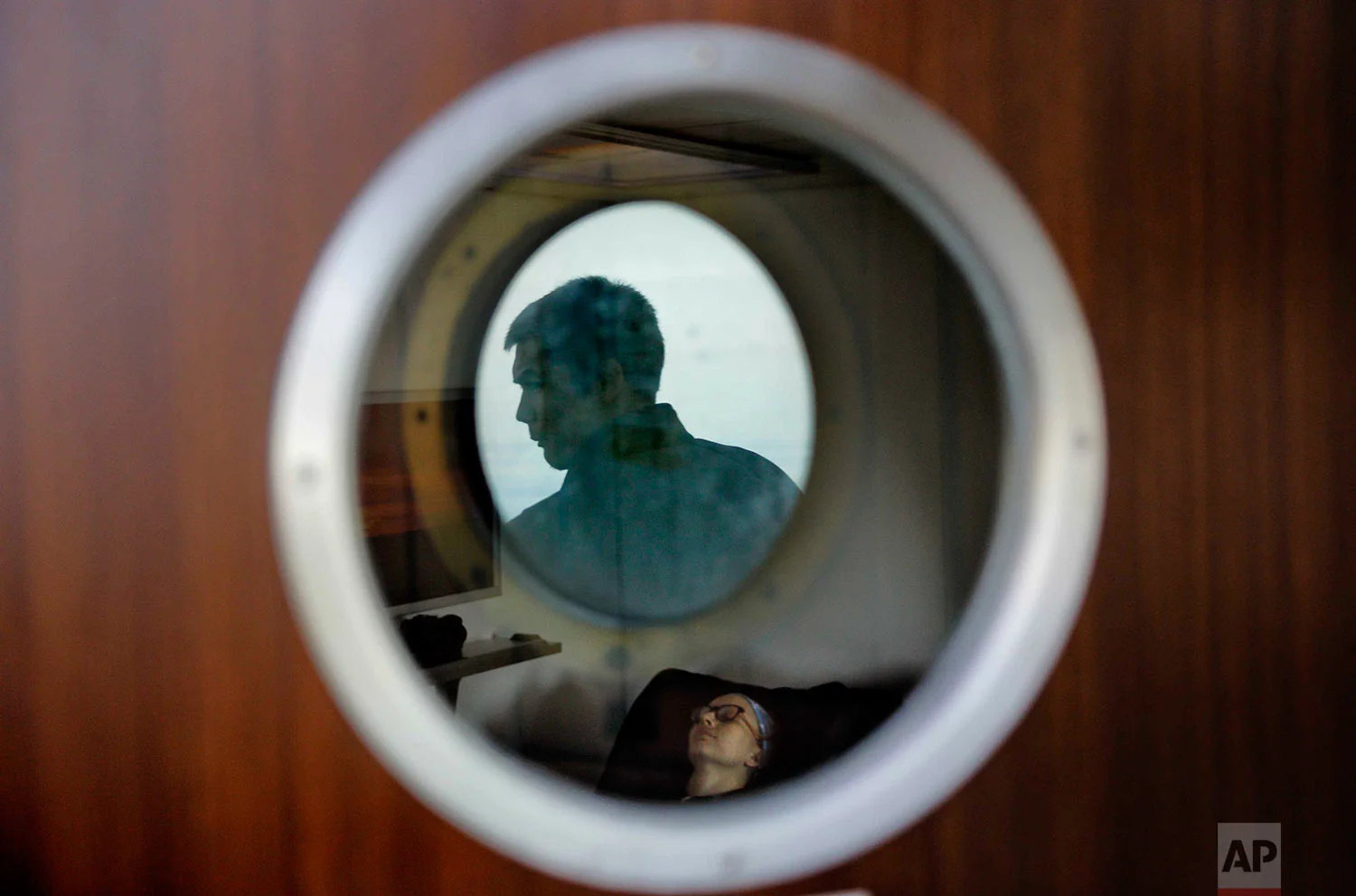 In this Thursday, July 13, 2017 photo, trainee David Kullualik is reflected in a deck door window looking out to sea as researcher Ilona Mettiainen reclines in a massage chair aboard the Finnish icebreaker MSV Nordica as it sails the Bering Sea to traverse the Northwest Passage through the Canadian Arctic Archipelago. (AP Photo/David Goldman)