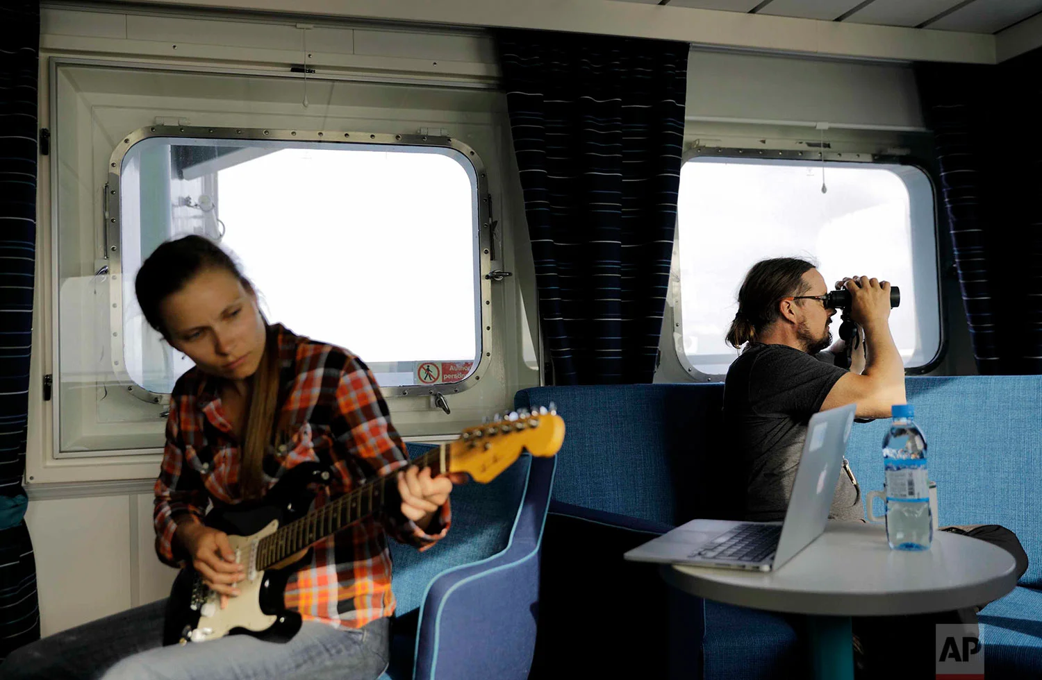 In this Friday, July 7, 2017 photo, researcher Daria Gritsenko, left, plays "Hotel California" on the guitar as fellow researcher Ari Laakso, right, looks from aboard the Finnish icebreaker MSV Nordica as it sails the North Pacific Ocean to traverse the Northwest Passage through the Canadian Arctic Archipelago. (AP Photo/David Goldman)