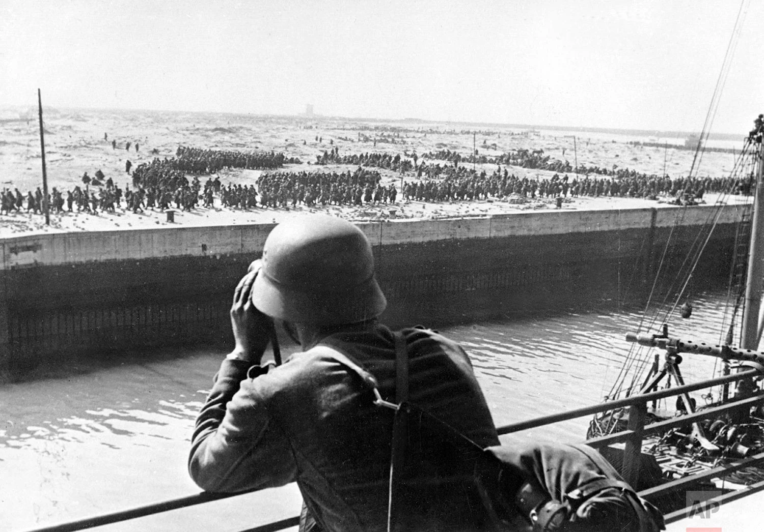 A member of the German Wehrmacht looks through a pair of binoculars on French and British prisoners of war in the harbor of Dunkirk on the Western Front in France, June 1940. (AP Photo/DPA)