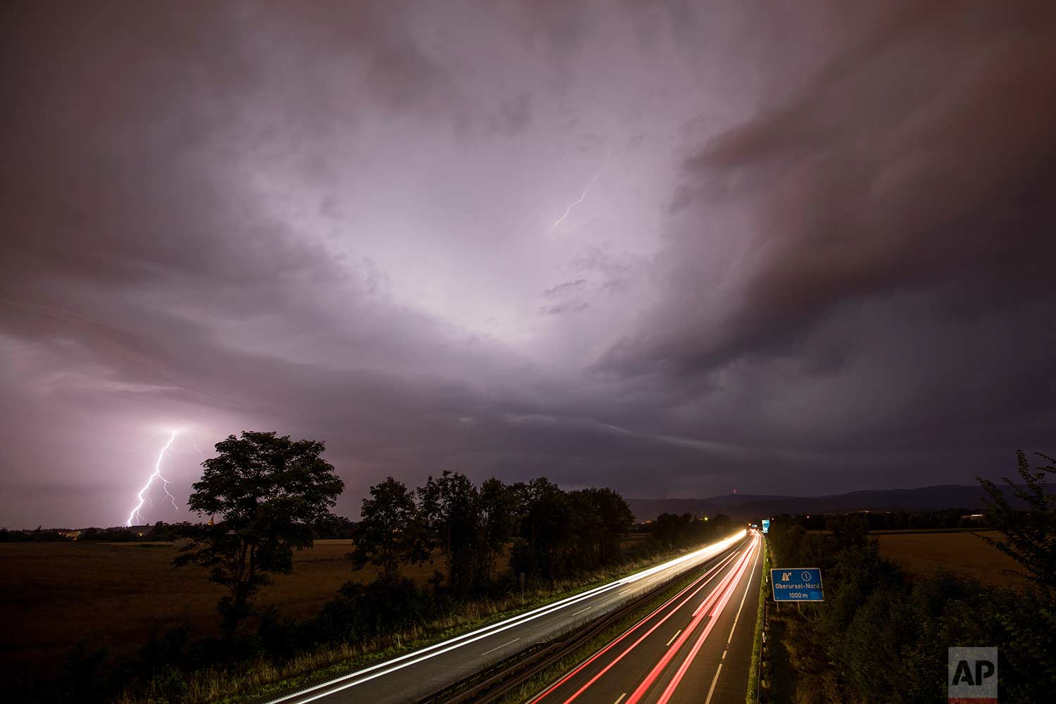 In this photo made with a long exposure, cars drive by as lightning strikes during thunderstorms in Oberursel, Germany, near Frankfurt on Saturday, July 22, 2017. (Jan Eifert/dpa via AP)