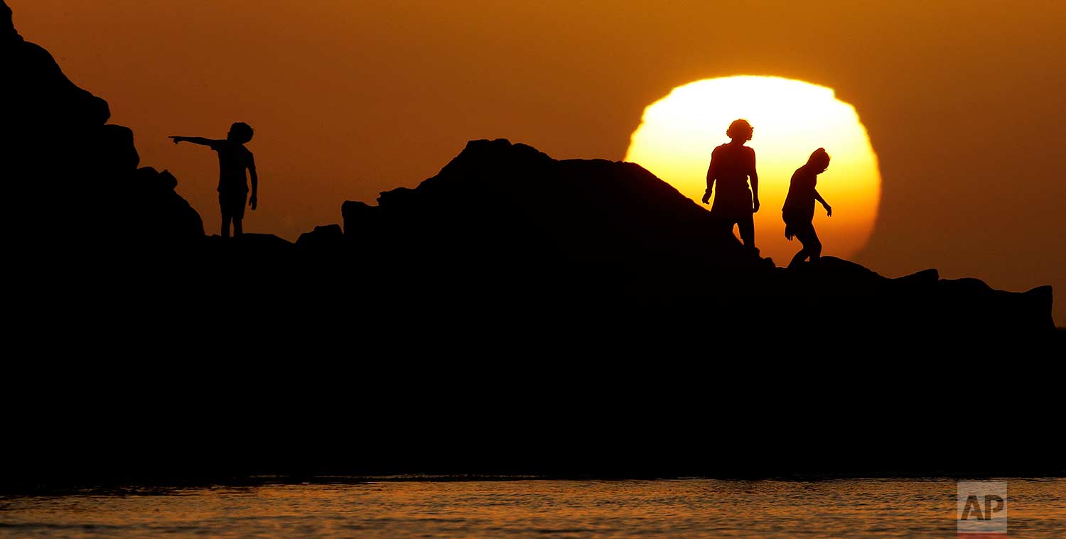 Kids play on rocks in Sunset Bay as the sun sets over the Pacific Ocean on Sunday, July 23, 2017, in Coos Bay, Ore. (AP Photo/Charlie Riedel)