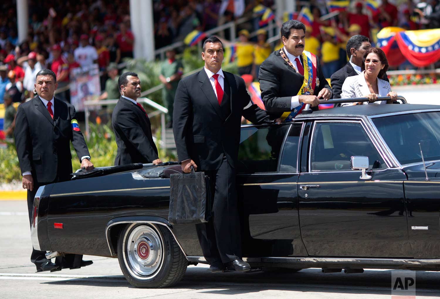 Venezuela’s President Nicolas Maduro and first lady Cilia Flores are surrounded by security guards during a military parade marking the one year anniversary of the death of Venezuela’s former President Hugo Chavez in Caracas, Venezuela. (AP Photo/Rodrigo Abd)