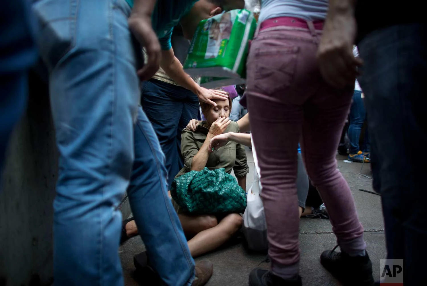 Irama Carrero is aided by fellow shoppers after fainting while waiting in a food line outside a grocery store, in the afternoon in Caracas, Venezuela. (AP Photo/Ariana Cubillos)