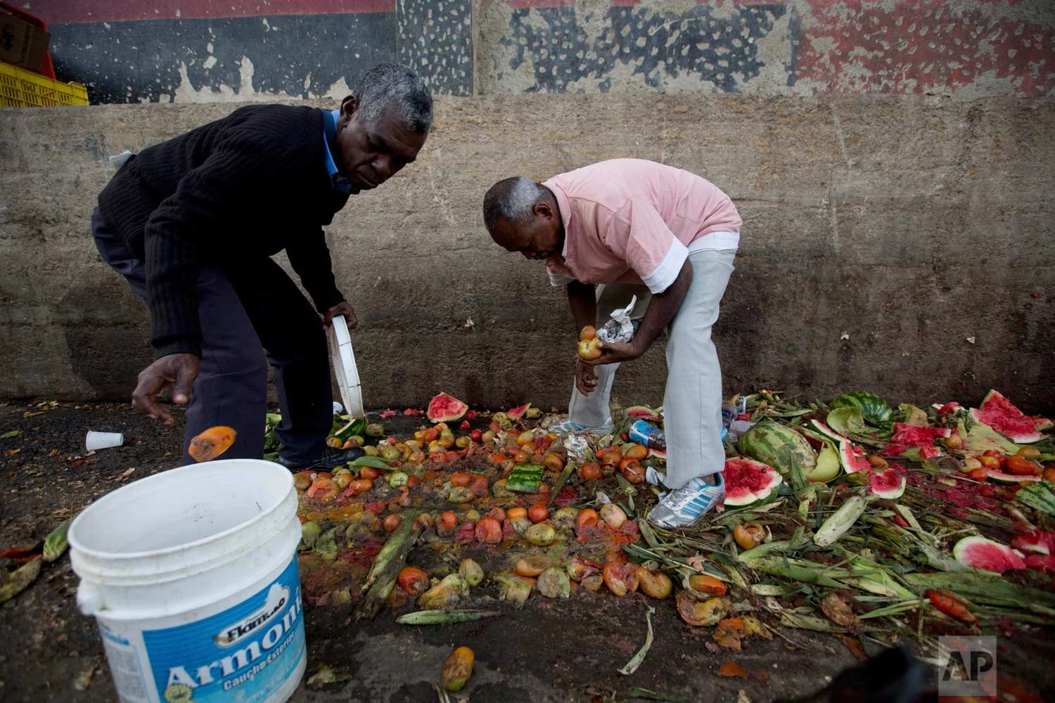 Pedro Hernandez, left, and his friend Luis Daza pick out tomatoes from the trash area of the Coche public market in Caracas, Venezuela. (AP Photo/Fernando Llano)