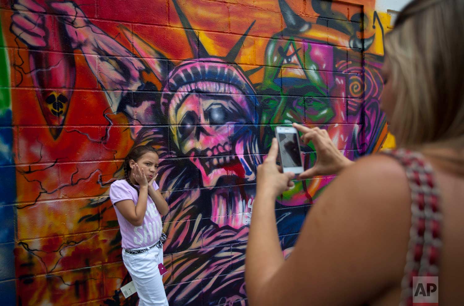 In this March 19, 2015 photo, a girl poses for a picture in front of a mural depicting the statue of liberty as death, at Bolivar square in Caracas, Venezuela. (AP Photo/Ariana Cubillos)