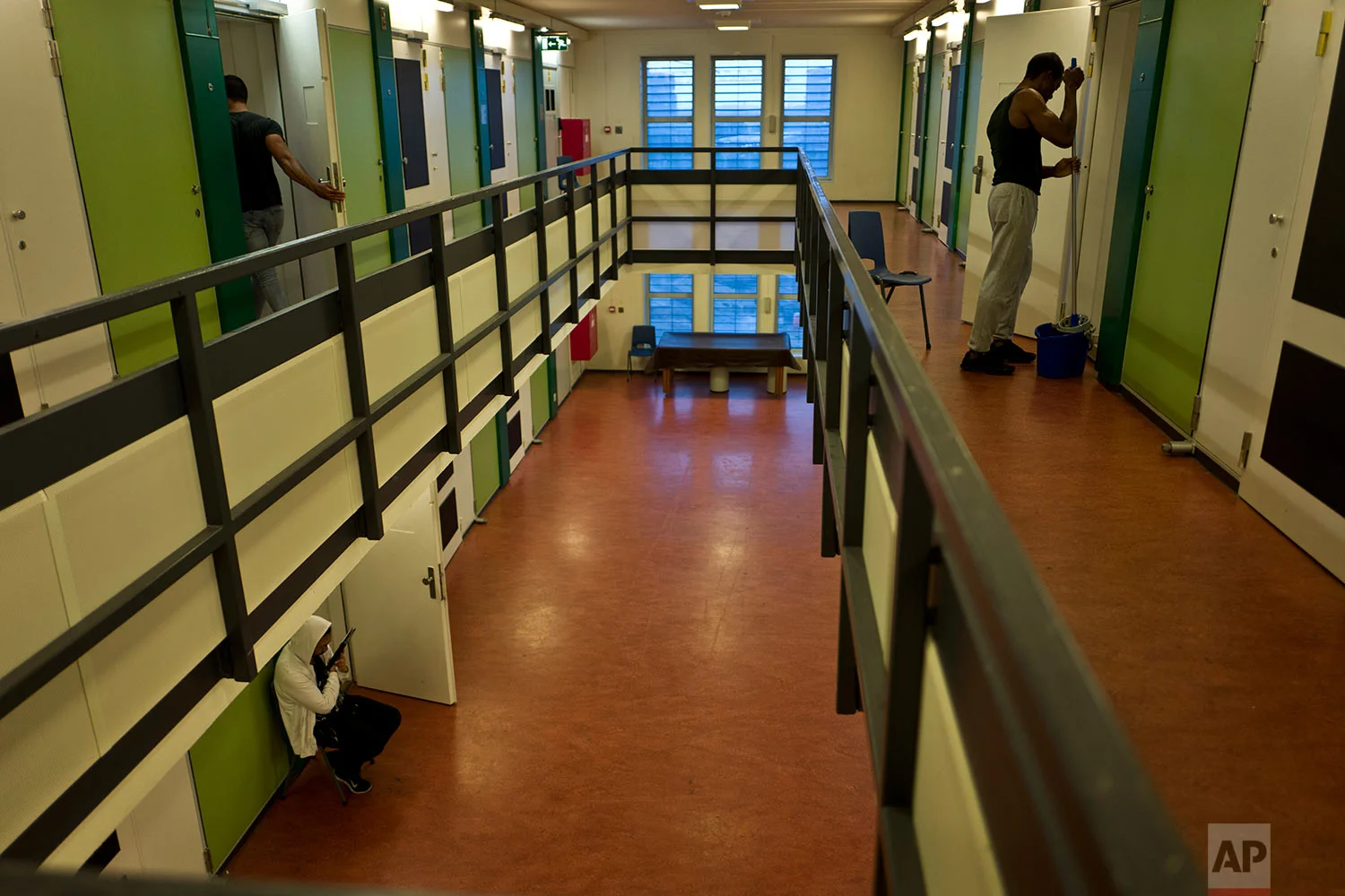 In this Saturday, July 29, 2017 photo, Angel John, 25, right, a migrant from Sierra Leone, cleans the ground in front of his room, while a Filipino migrant, bottom left, sits by the doorway of his room at the former prison of Bijlmerbajes in Amsterdam, Netherlands. (AP Photo/Muhammed Muheisen)