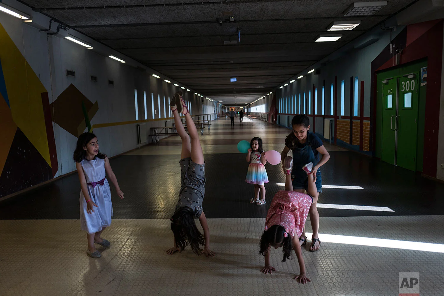 In this Wednesday, July 19, 2017 photo, Syrian refugee girls, from left, Shahd Alamar, 8, Lana Alkhawaja, 9, Maya Alamar, 4, holding balloons, Amal Sakkal, 8, and Hala Alhalaby, 8, play in a corridor known as Kalverstraat, referring to a busy shopping street in Amsterdam, at the former prison of Bijlmerbajes in Amsterdam, Netherlands. (AP Photo/Muhammed Muheisen)