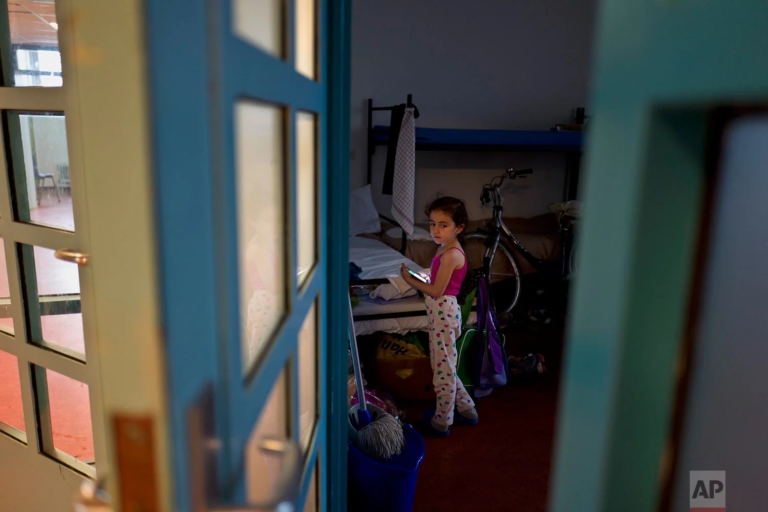 In this Friday, June 30, 2017 photo, refugee Sandi Yazji, 5, from al-Hasaka, Syria, holds a mobile phone while standing inside her room at the former prison of Bijlmerbajes in Amsterdam, Netherlands. (AP Photo/Muhammed Muheisen)