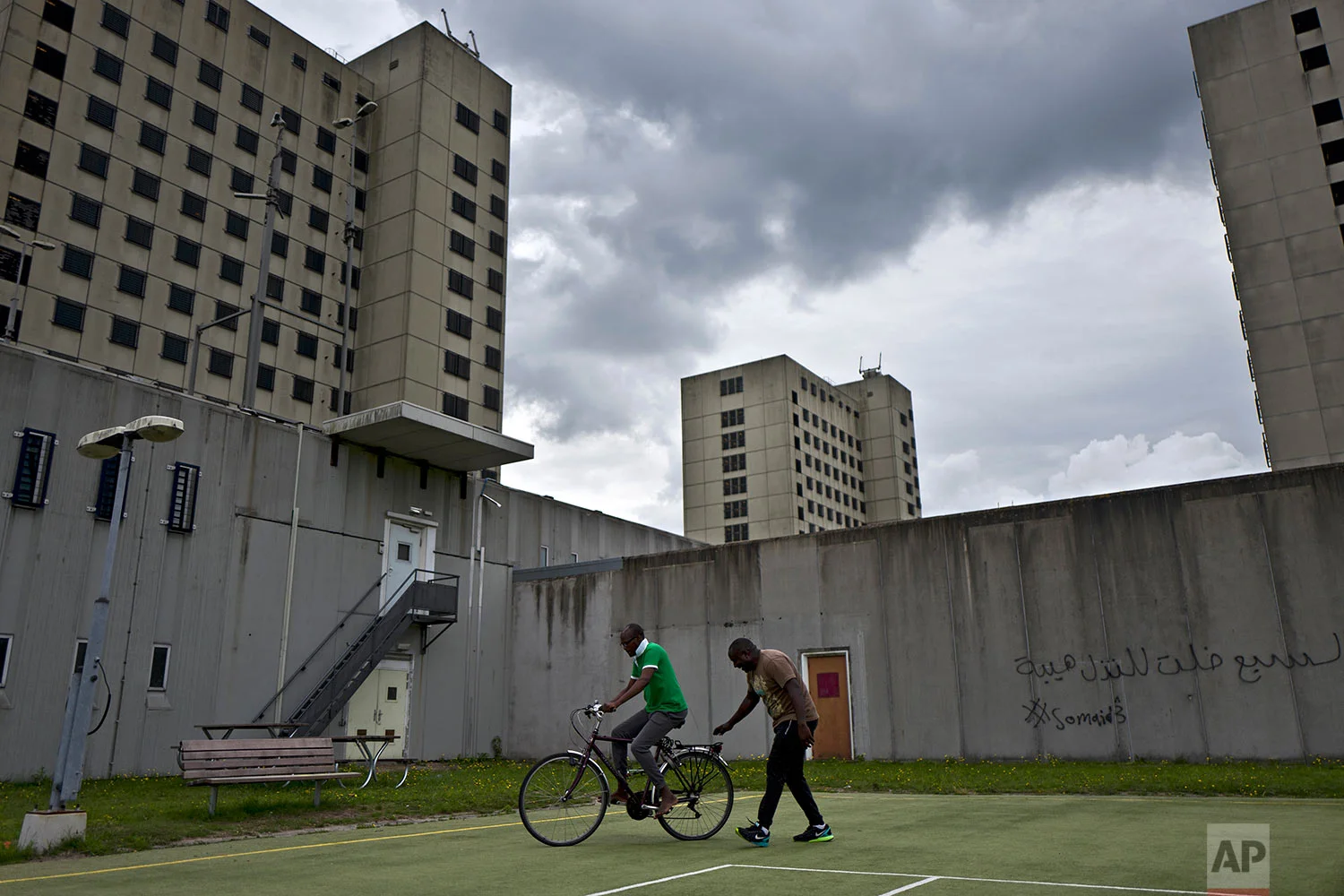 In this Monday, July 3, 2017 photo, Aimable Nasbimana, 37, right, a migrant from Burundi, teaches his Congolese friend Prosper Baseka, 37, how to ride a bicycle in a yard at the former prison of Bijlmerbajes in Amsterdam, Netherlands. (AP Photo/Muhammed Muheisen)