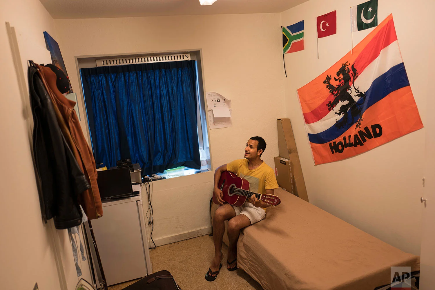 In this Sunday, July 16, 2017 photo, Rawaiz Bhatti, 26, a migrant from Peshawar, Pakistan, plays guitar and sings in his room at the former prison of Bijlmerbajes in Amsterdam, Netherlands. (AP Photo/Muhammed Muheisen)