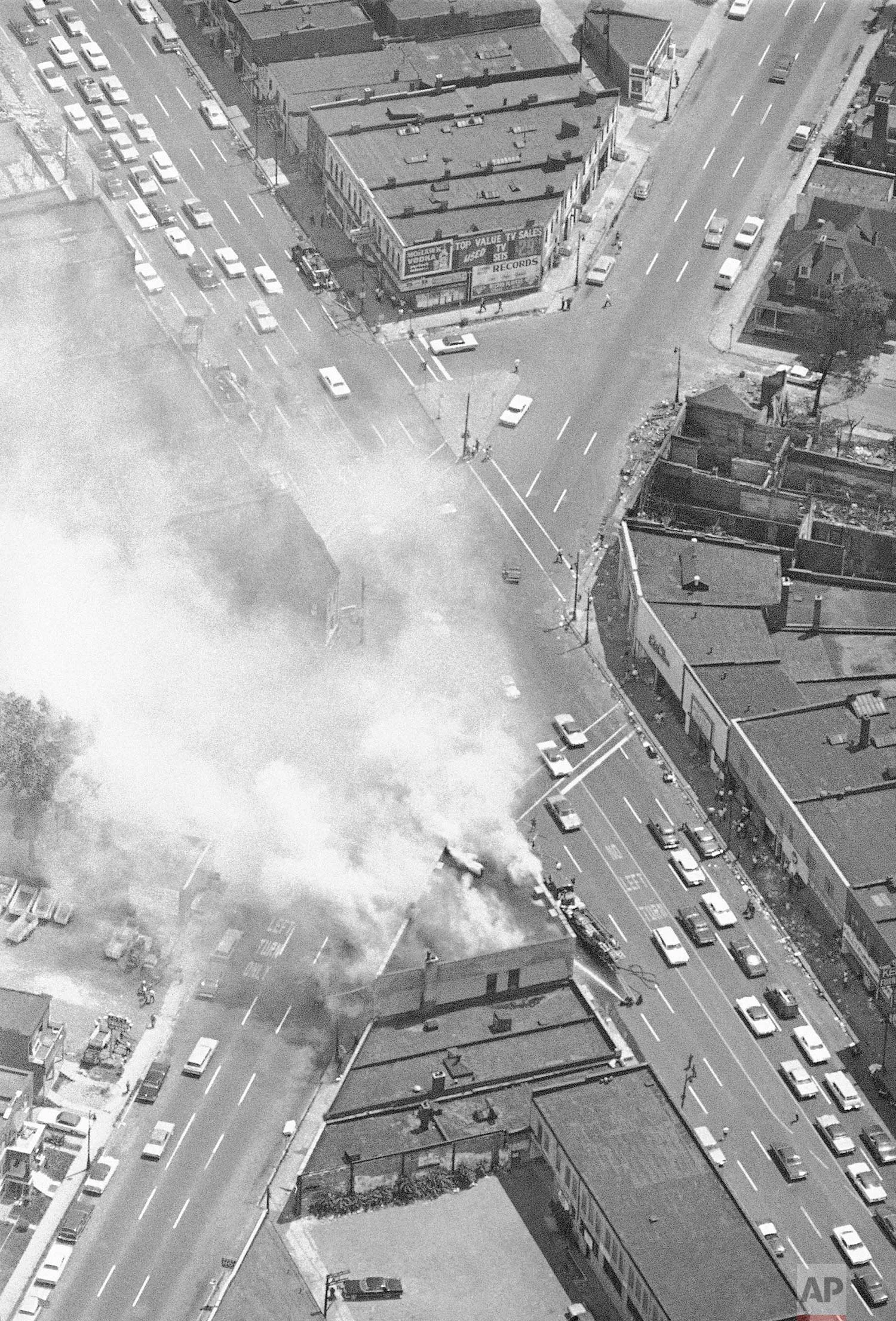 In this July 25, 1967 photo, smoke rises from a fire set at the busy intersection of Grand River and 14 Street in Detroit, near another burned out building. The fire was set despite patrols by the National Guard, police and Army troops. (AP Photo)