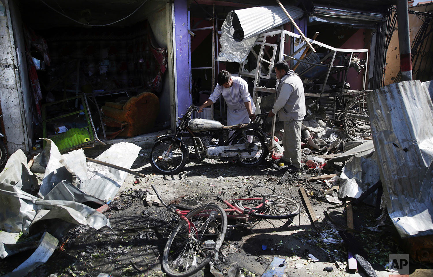 Men look at the remains of their properties at the site of a suicide attack in Kabul, Afghanistan, Monday, July 24, 2017. A suicide car bomb killed dozens of people as well as the bomber early Monday morning in a western neighborhood of Afghanistan'