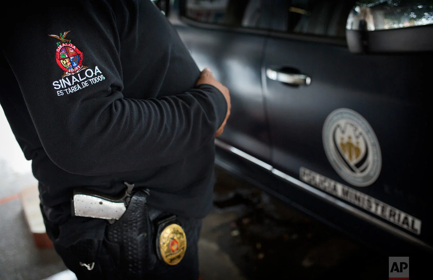 In this June 28, 2017 photo, a police officer stands outside Riodoce's office in Culiacan, Sinaloa state, Mexico. After the killing of Riodoce co-founder Javier Valdez, two police were assigned by the state government to guard the newspaper's offices. Half-jokingly, some of the reporters wondered whether these officers are among the 50 percent of cops whom the governor himself has said are not trustworthy. The badge on the police officer's sleeve reads, in Spanish, "Sinaloa is everyone's task." (AP Photo/Enric Marti)