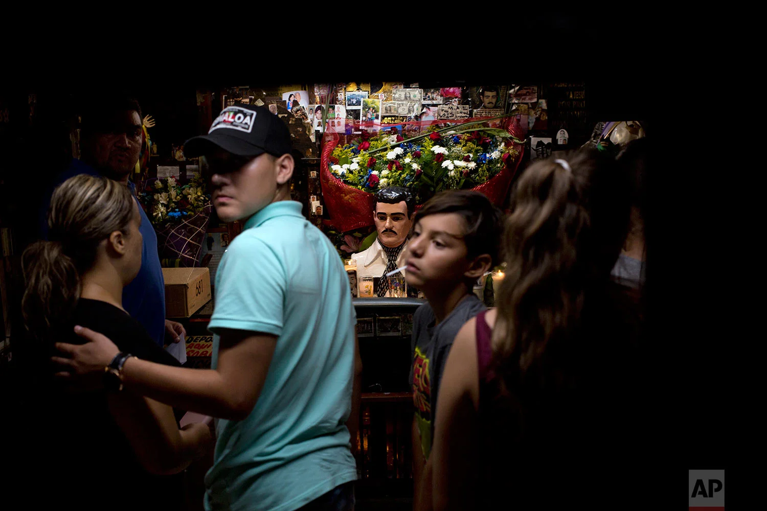 In this June 27, 2017 photo, a family from the United States visits the shrine of Jesus Malverde, the so-called narco-saint revered by many of Mexico's drug traffickers, in Culiacan, Sinaloa state, Mexico. In Sinaloa people are shot dead in the street every day and the cemetery is filled with ornate, two-story mausoleums for drug kings that are larger than many homes for the living. (AP Photo/Enric Marti)