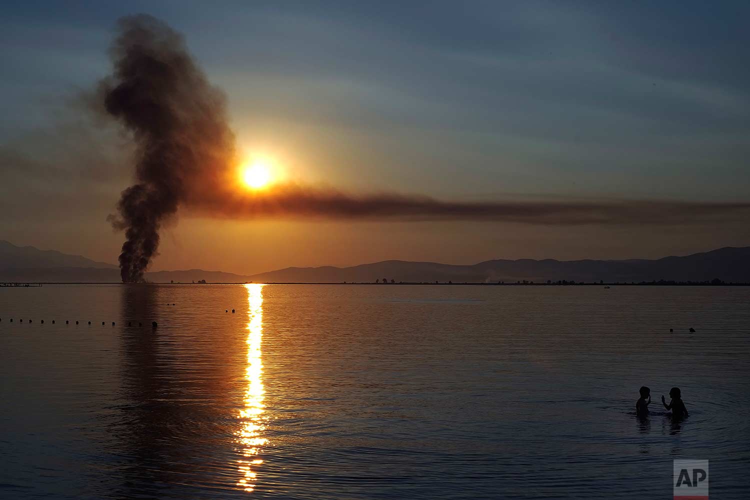  Children play in the sea as smoke from a fire rises in the background during a sunset at Keramoti, northern Greece, on Sunday, July 30, 2017. (AP Photo/Petros Karadjias) 