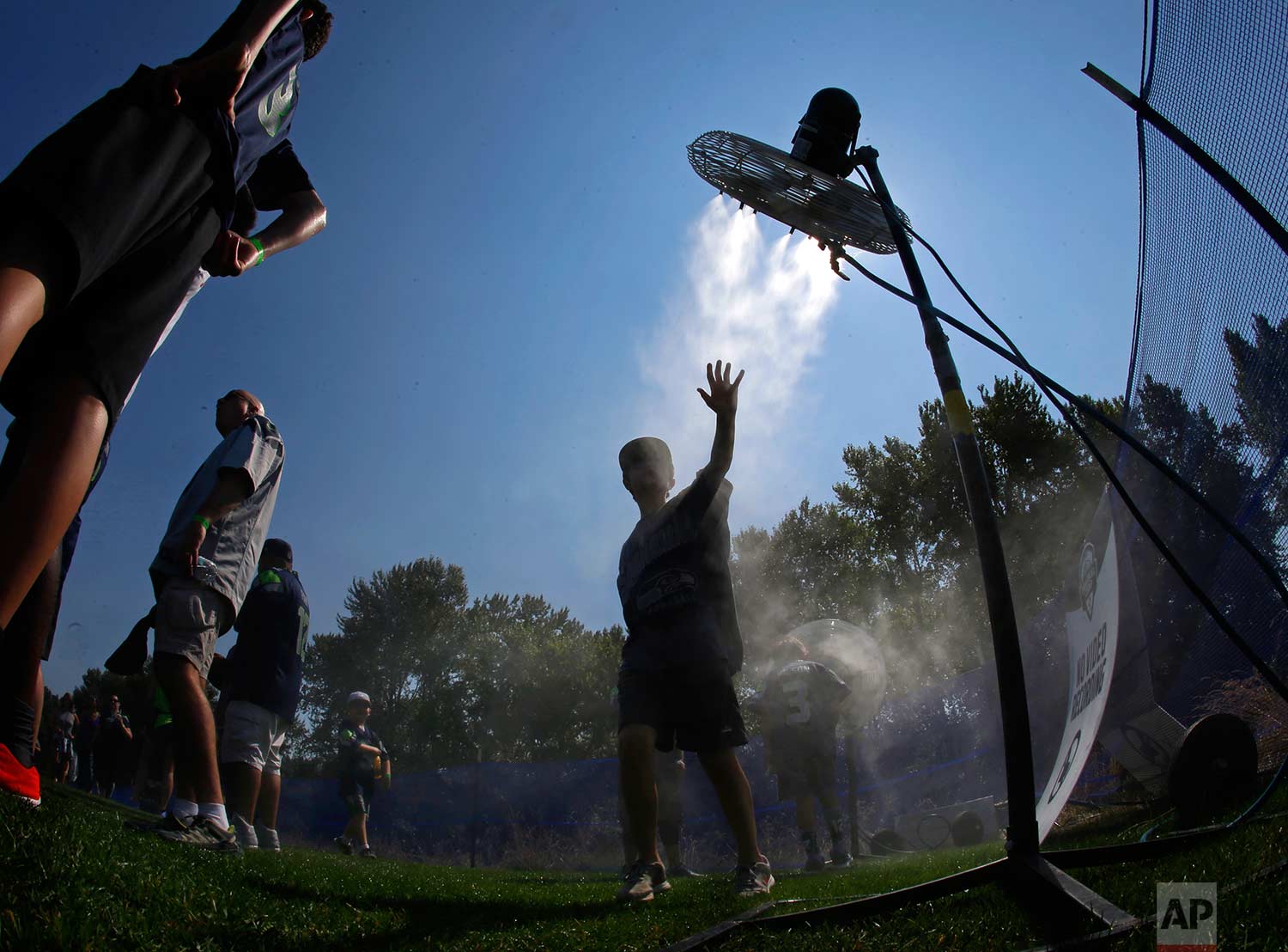  A fan attending a Seattle Seahawks NFL football training camp reaches toward a fan as he cools off at a misting station, Tuesday, Aug. 1, 2017, in Renton, Wash. (AP Photo/Ted S. Warren) 