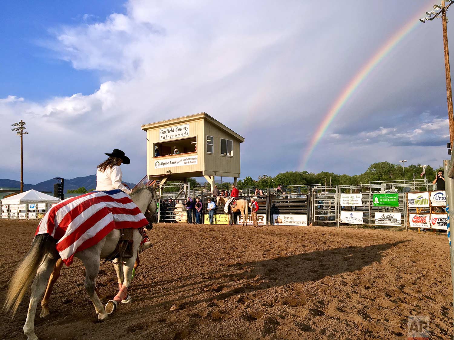  A flag-draped riderless horse to honor the fallen is led through the arena at the Garfield County Fair and Rodeo in Rifle, Colo., as a rainbow arcs in the background. (Chelsea Self/Glenwood Springs Post Independent via AP) 