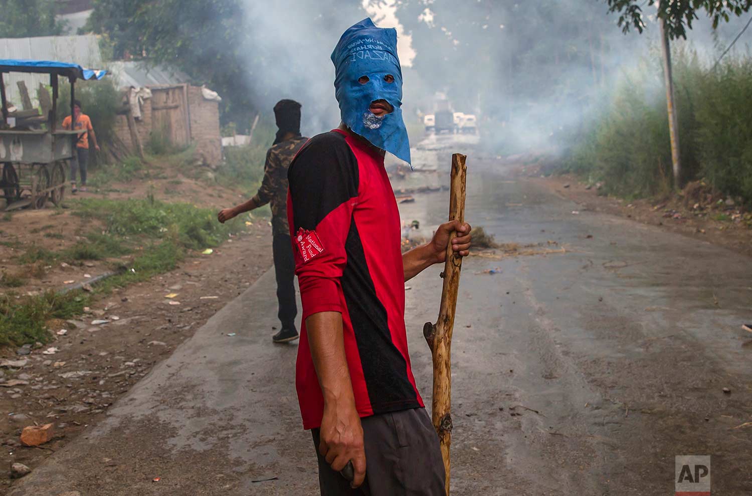  A masked villager holds a wooden stick and stones during a protest following the funeral procession of Akeel Ahmed Bhat, a teenage boy in Haal village, about 47 kilometers (29 miles) south of Srinagar, Indian controlled Kashmir, Wednesday, Aug. 2, 2