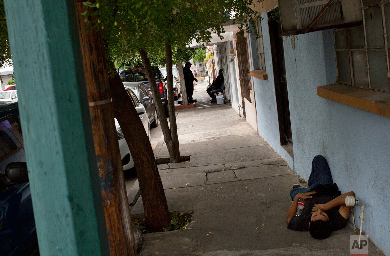 In this June 28, 201 photo, police, behind, sit in the shade as a man rests on the sidewalk outside Riodoce's office in Culiacan, Sinaloa state, Mexico. The police were assigned to this post after the killing of Riodoce reporter Javier Valdez by the state government to guard Riodoce's offices, housed in a apartment building in a middle-class neighborhood of Culiacan. Half-jokingly, some of the reporters wondered whether these officers are among the 50 percent of cops whom the governor himself has said are not trustworthy. (AP Photo/Enric Marti)