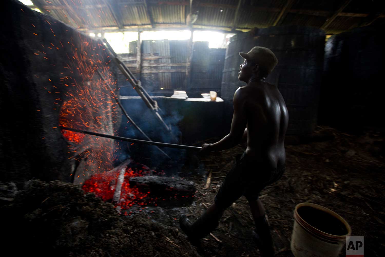 In this June 16, 2017 photo, Batel Delciner, 23, removes wood from a furnace to lower the heat cooking sugar juice at the Ti Jean distillery, which produces clairin, a sugar-based alcoholic drink, in Leogane, Haiti. (AP Photo/Dieu Nalio Chery)