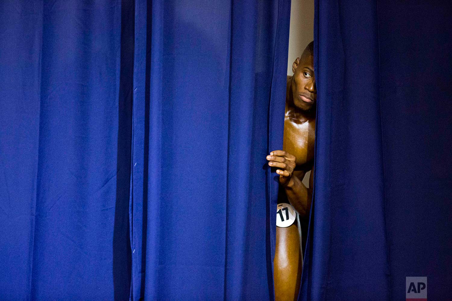 In this July 23, 2017 photo, a Haitian bodybuilder peers from behind the curtain to watch his competitors perform at the Haiti Bodybuilding Classic, an event with Haitian and Dominican Republic athletes, in Port-au-Prince, Haiti. (AP Photo/Dieu Nalio Chery)