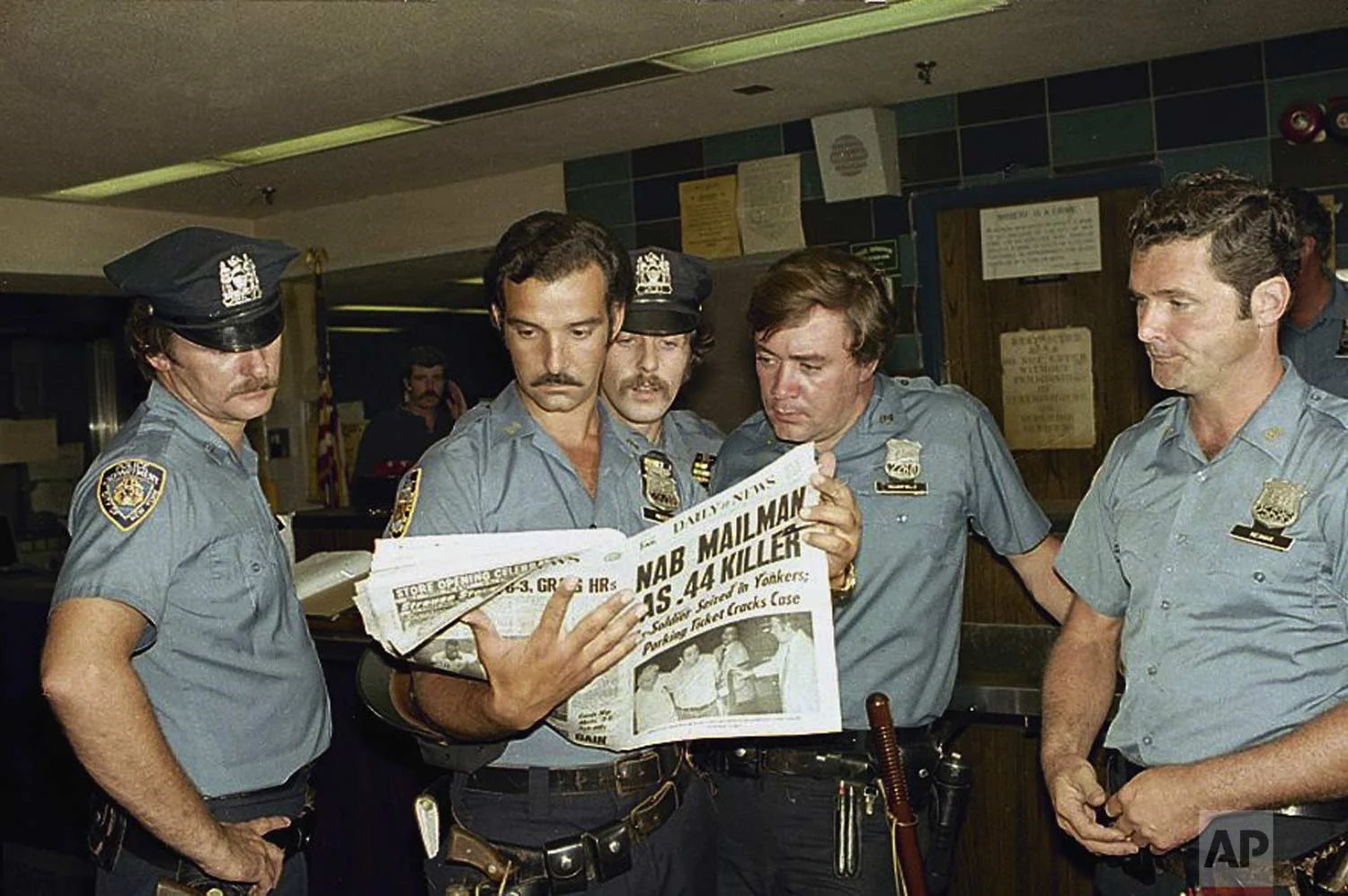 Unidentified officers of the 84th Precinct in Brooklyn read news of the capture of the “.44 Caliber Killer”, David Berkowitz, Aug. 11, 1977. (AP Photo/Dan Goodrich)