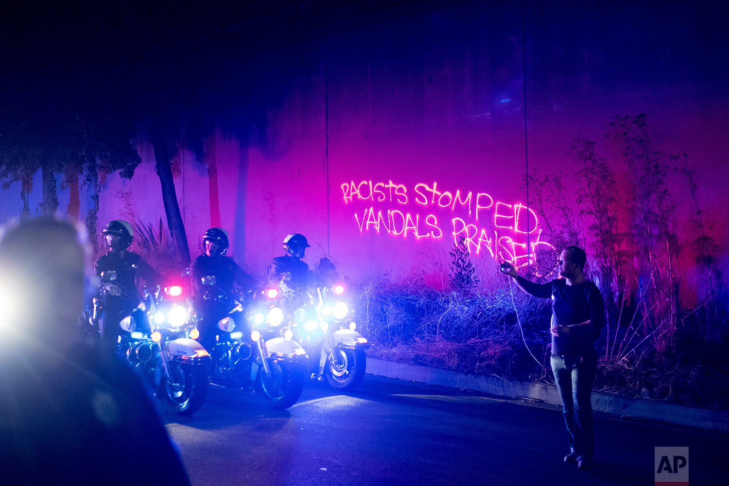  Graffiti spray-painted by a protester lines a wall as police officers clear demonstrators from a freeway off-ramp in Oakland, Calif., Saturday, Aug. 12, 2017. (AP Photo/Noah Berger) 