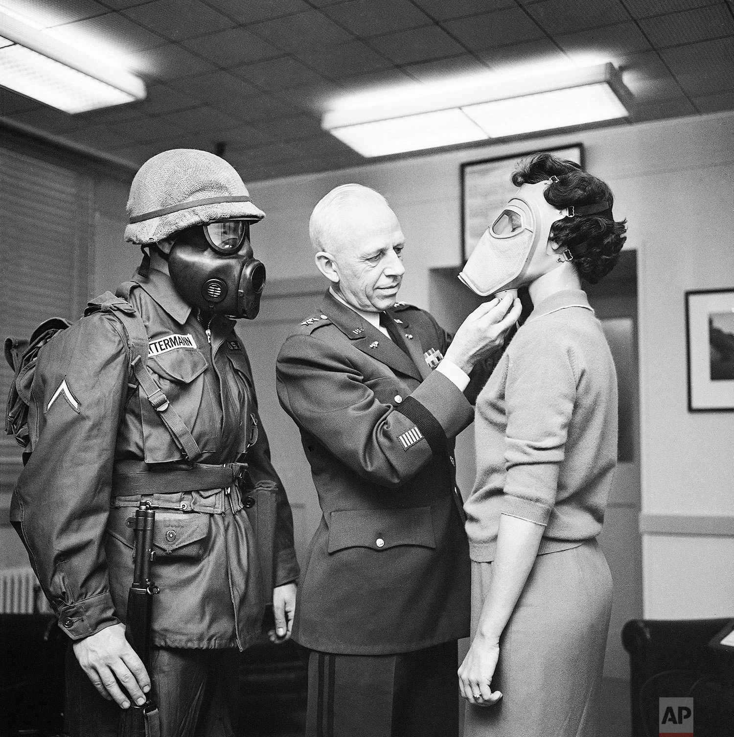In this Jan. 19, 1959 photo, Pfc. Warner Bitterman, left, watches as Army chief chemical officer Maj. Gen. Marshall Stubbs, center, checks new civilian gas mask being worn secretary Margaret Francis at his Pentagon office in Washington. (AP Photo)