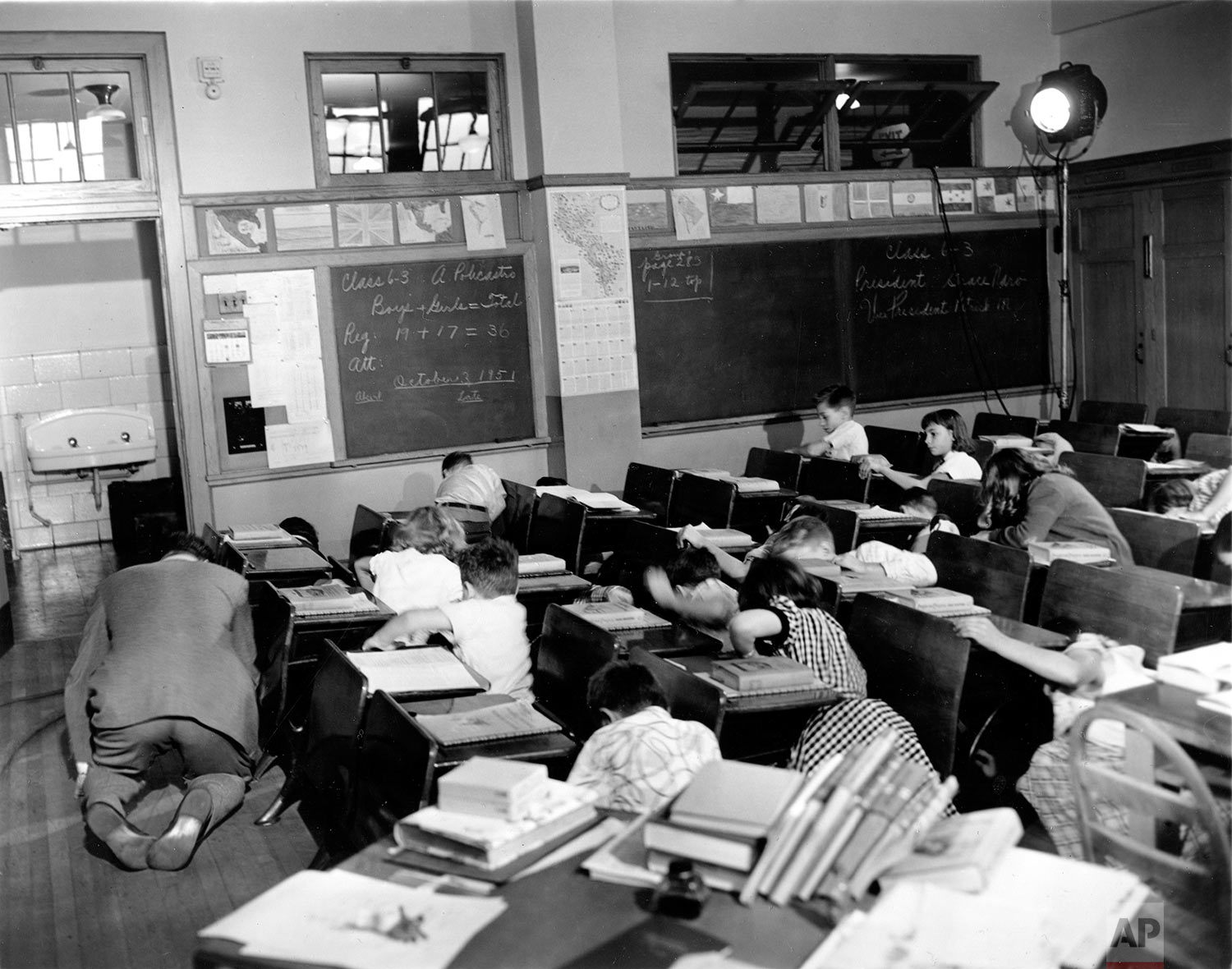  In this Nov. 21, 1951 picture, sixth grade students crouch under or beside their desks along with their teacher, Vincent M. Bohan, left, as they act out a scene from the Federal Civil Defense administration film "Duck and Cover" at Public School 152 in the Queens borough of New York City. Even before the March 11 earthquake and resulting tsunami that led to the Japanese nuclear crisis, Americans were bombarded with contradictory images and messages that frighten even when they try to reassure. It started with the awesome and deadly mushroom cloud rising from the atomic bomb, which led to fallout shelters and school duck-and-cover drills. (AP Photo/Dan Grossi)