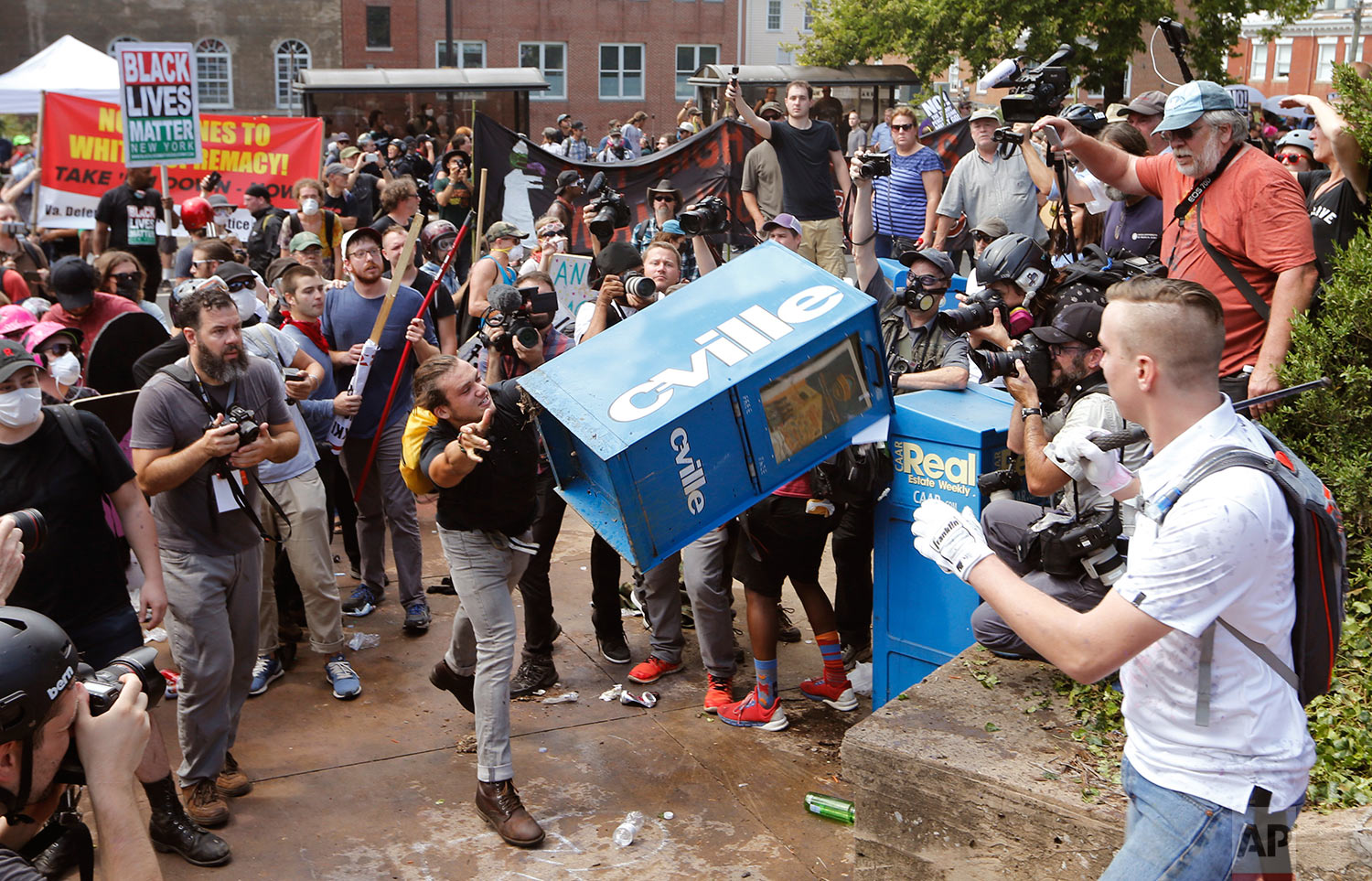 White nationalist demonstrators clash with a counter demonstrator  as he throws a newspaper box at the entrance to Lee Park in Charlottesville, Va., Saturday, Aug. 12, 2017. Gov. Terry McAuliffe declared a state of emergency and police dressed in ri