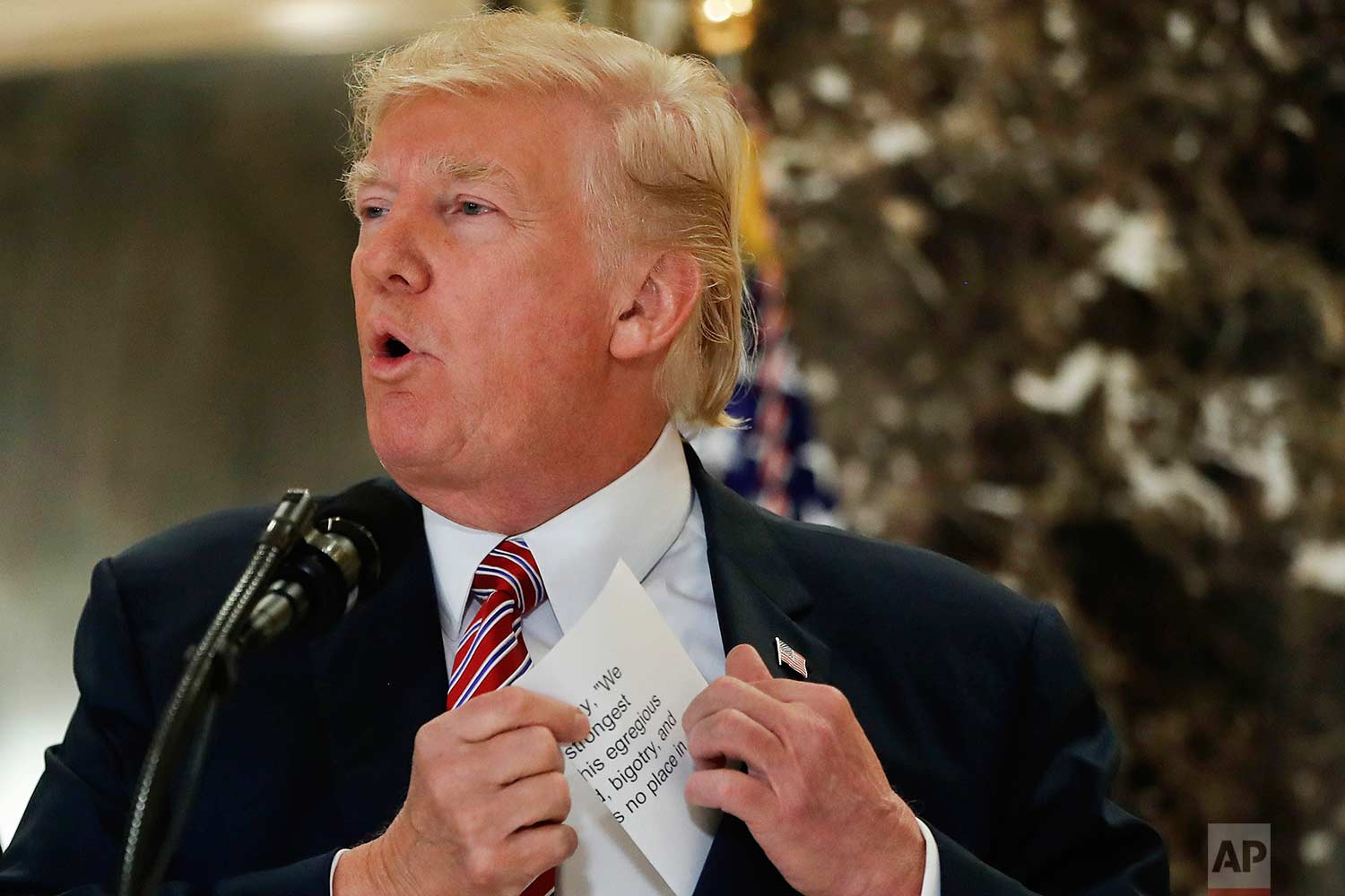  President Donald Trump reaches into his suit jacket Tuesday, Aug. 15, 2017 to read a quote he made on Saturday, Aug. 12, regarding the events in Charlottesville, Va., as he speaks to the media in the lobby of Trump Tower in New York. (AP Photo/Pablo
