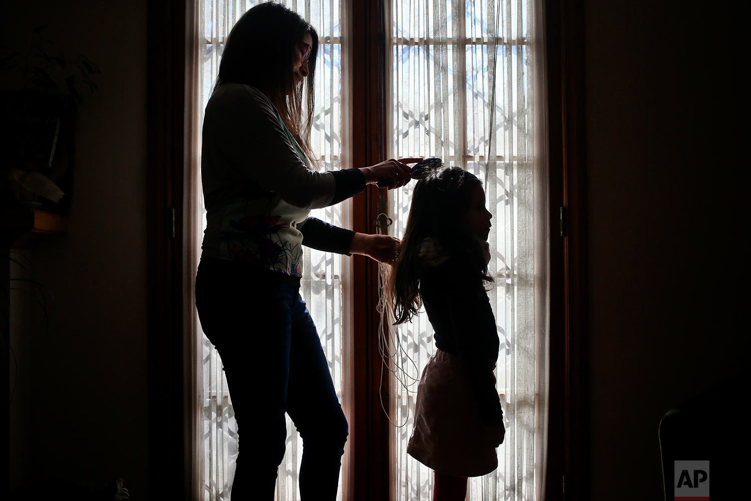  In this July 18, 2017 photo, Monica Flores combs her daughter's hair at their home in Santiago, Chile. Flores was questioned by Chilean police at the airport because the records didn't match: she had left on holidays abroad with a son and returned t