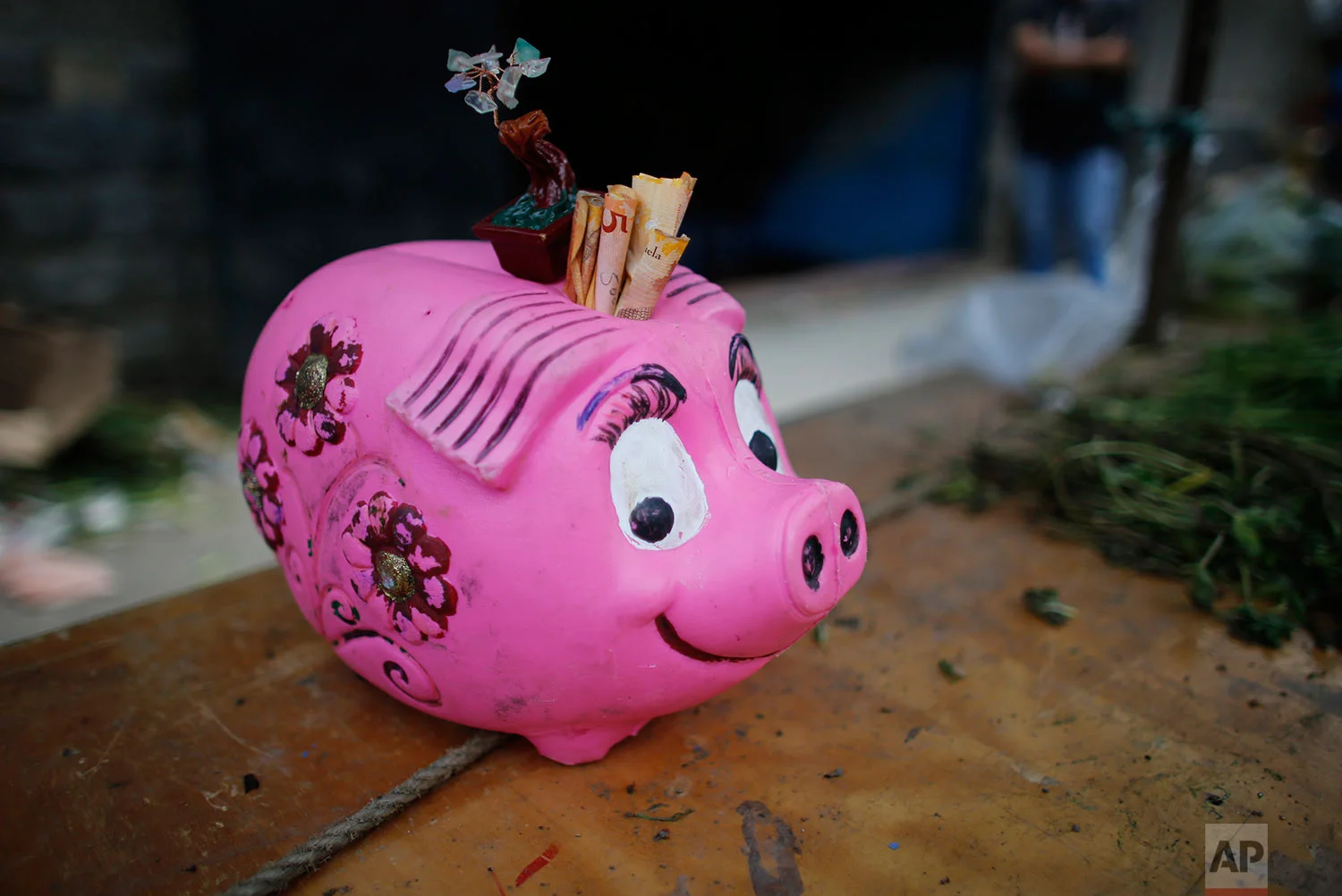 A piggy bank for tips, filled with 5 Bolivar bills, sits on the table of a vegetable vendor at a market, Aug. 23, 2017, Caracas, Venezuela. (AP Photo/Ariana Cubillos)