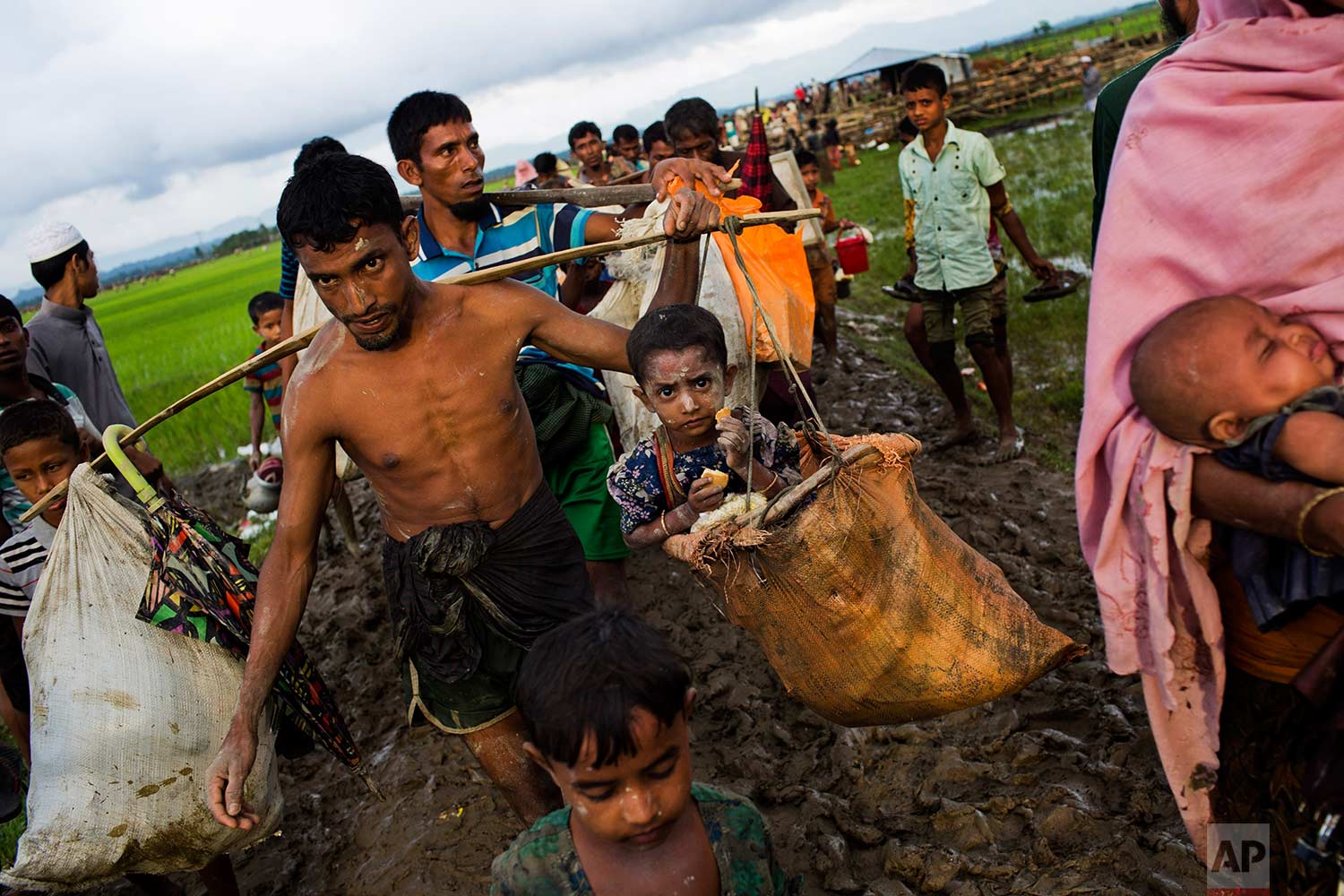 A Rohingya ethnic minority refugee from Myanmar carries a child in a sack and walks through rice fields after crossing over to the Bangladesh side of the border near Cox's Bazar's Teknaf area, Friday, Sept. 1, 2017. Myanmar's military says almost 400 people have died in recent violence in the western state of Rakhine triggered by attacks on security forces by insurgents from the Rohingya. (AP Photo/Bernat Armangue)