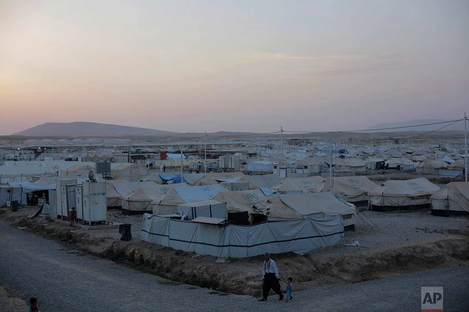 In this Wednesday, Aug. 2, 2017 photo, a man walks with a child through the Hassan Sham camp in Northern Iraq. (AP Photo/Bram Janssen)