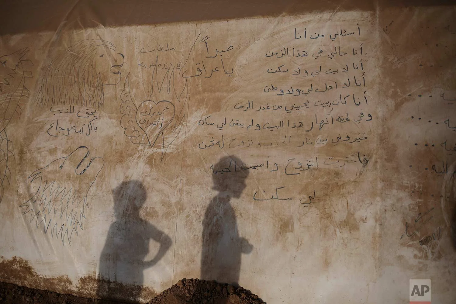 In this Sunday, July 25, 2017 photo, the shadows of two boys are seen on the side of a tent inside the Khazer camp for displaced people in Northern Iraq. A poem is written in the side of the tent: "Ask me who I am, I am talking for myself. I am the one who doesn't have a house or a home. I'm the one without relatives and a country. I used to have a house protecting me from the treason of time. In a moment this house collapsed and there's something left for me. I had to choose between the flames of war and the consequences of displacement. I chose displacement and the tent became my home." (AP Photo/Bram Janssen)