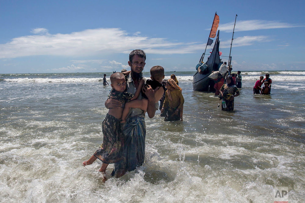  A Rohingya Muslim man walks to shore carrying two children after they arrived on a boat from Myanmar to Bangladesh in Shah Porir Dwip, Bangladesh, Thursday, Sept. 14, 2017. Those who arrived Wednesday in wooden boats described ongoing violence in My