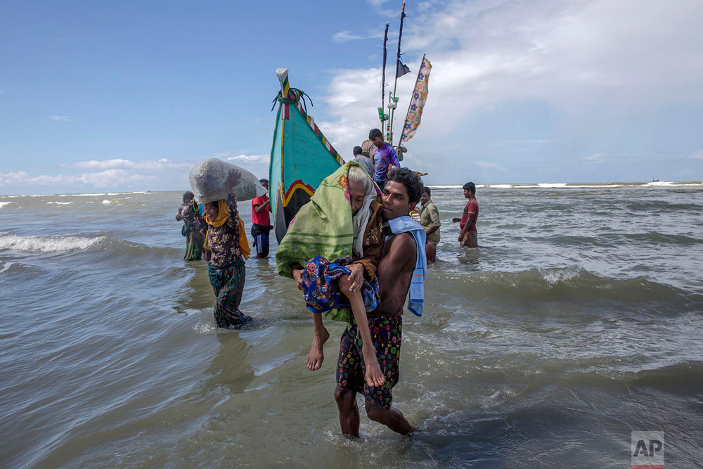  A Rohingya Muslim man walks to shore carrying an elderly woman after they arrived on a boat from Myanmar to Bangladesh in Shah Porir Dwip, Bangladesh, Thursday, Sept. 14, 2017. Nearly three weeks into a mass exodus of Rohingya fleeing violence in My