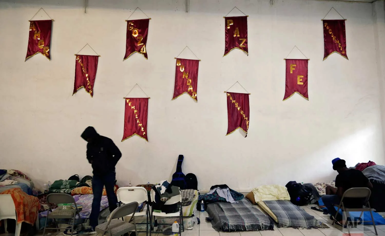 In this May 24, 2017 photo, Haitian men gather before sleeping below inspirational banners written in Spanish at The Ambassadors of Jesus Church in Tijuana, Mexico. (AP Photo/Gregory Bull)