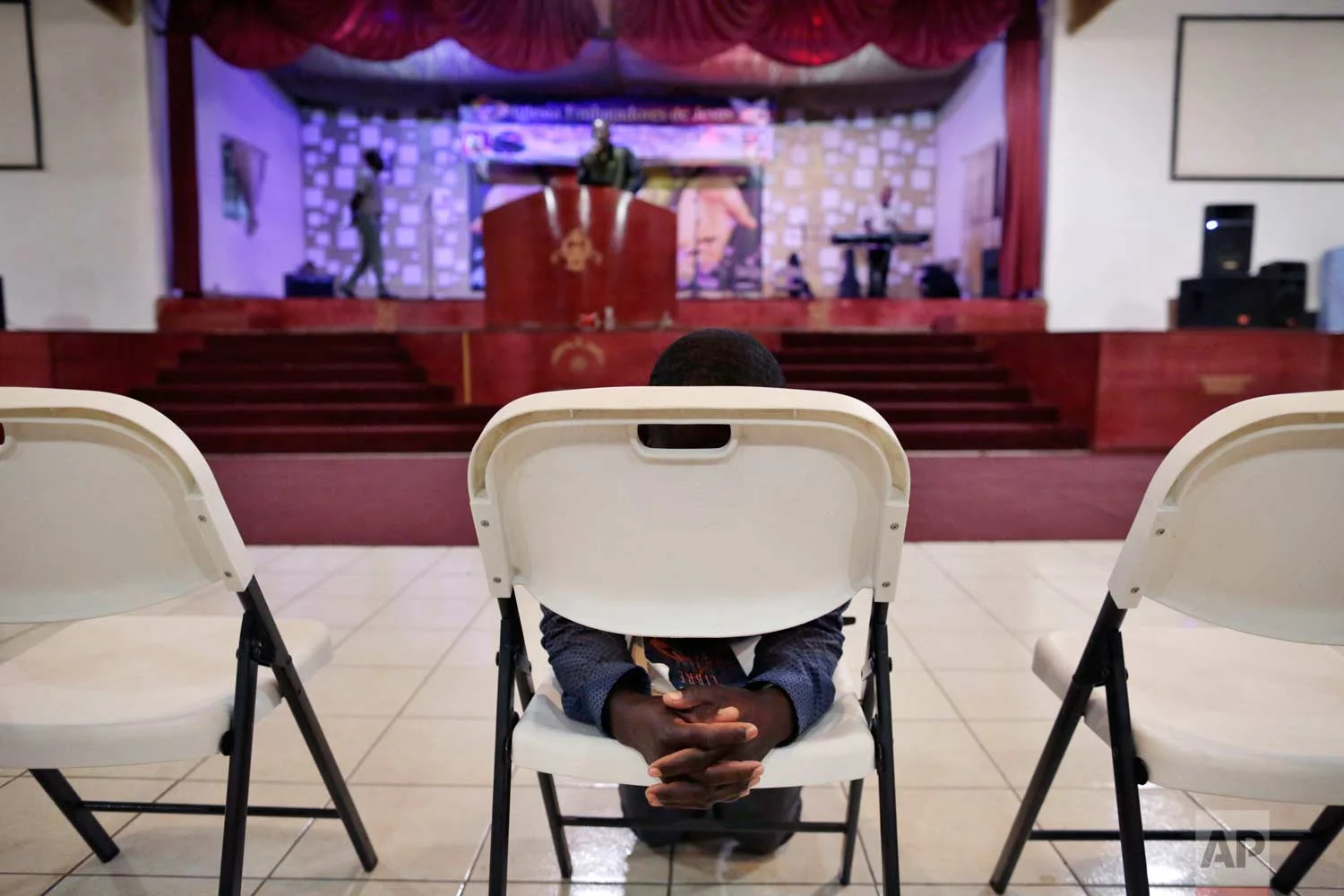 In this May 24, 2017 photo, Jeccene Thimote, of Haiti, kneels in front of a folding chair in prayer during a service in Creole at The Ambassadors of Jesus Church in Tijuana, Mexico. (AP Photo/Gregory Bull)