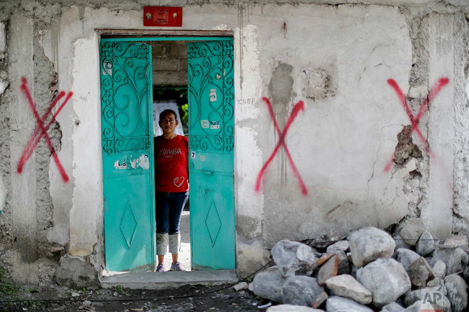 Nadia Rosas stands inside her aunt's home covered with spray paint symbols designating it condemned, after it was destroyed by an earthquake, Sept. 23, 2017, in Atzala, Mexico. Rosas moved in with her 68-year-old aunt after the earthquake destroyed everything. "In these catastrophes we're united as brothers, as people, as women," Rosas said. (AP Photo/Natacha Pisarenko)