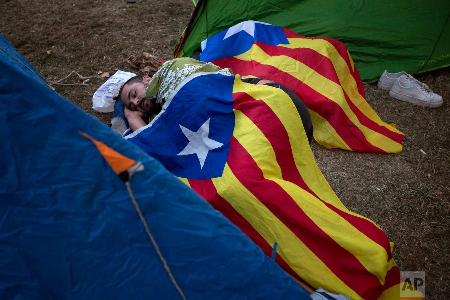 In this photo taken on Friday, Sept. 22, 2017, people sleep on the ground covered with the "estelada" or independence flags, during a protest in Barcelona, Spain. (AP Photo/Emilio Morenatti)