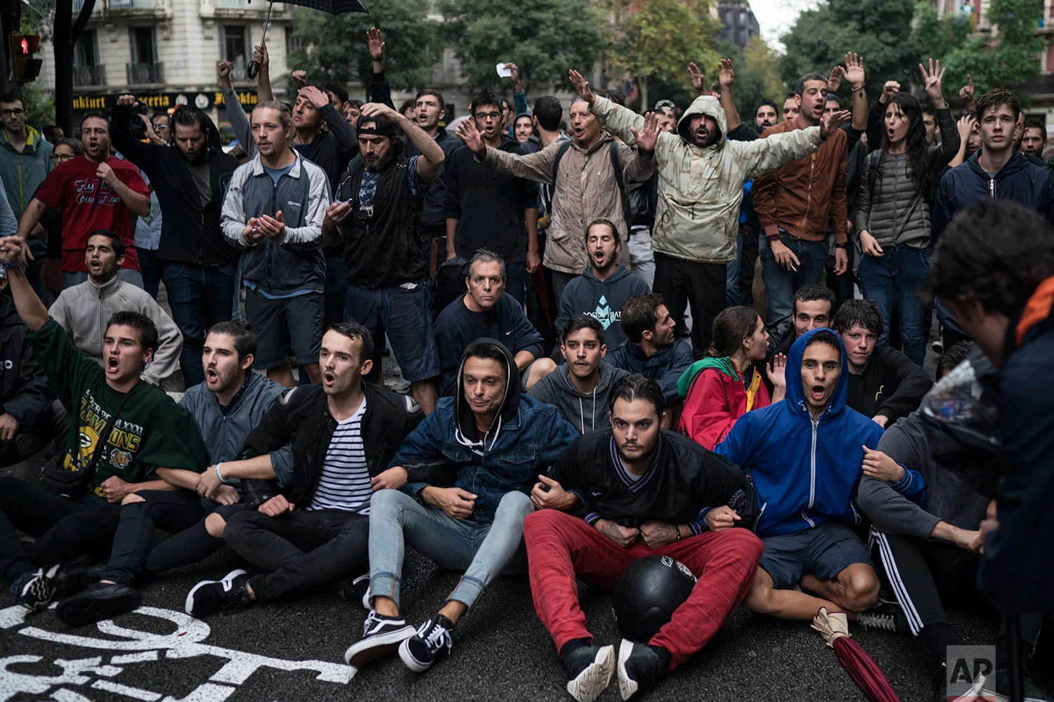 People sits in the middle of the street to block Spanish riot police near a voting site at a school assigned to be a polling station by the Catalan government in Barcelona, Spain, Sunday, 1 Oct. 2017. Catalan pro-referendum supporters vowed Saturday to ignore a police ultimatum to leave the schools they are occupying to use in a vote seeking independence from Spain. (AP Photo/Felipe Dana)