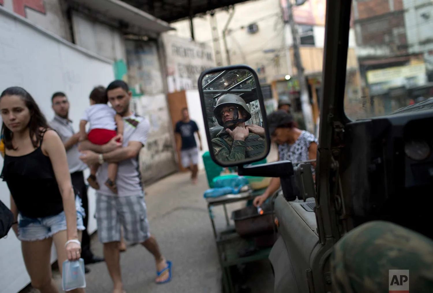 In this Sept. 28, 2017 photo, residents walk past an armored vehicle at the Rocinha slum, in Rio de Janeiro, Brazil. Nearly 1,000 troops were sent in, in mid-September as shootings erupted in Rocinha and other slums across the city. Schools cancelled classes and roads were closed as many feared the violence could escalate. (AP Photo/Silvia Izquierdo)